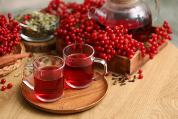 Cups of tasty viburnum tea on wooden table in room, closeup