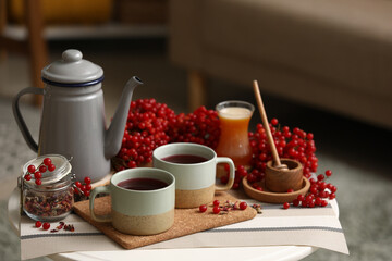 Teapot and cups of tasty viburnum tea on table in interior of living room, closeup