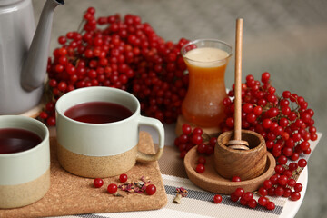Bowl of honey and cups of tasty viburnum tea on table in living room, closeup