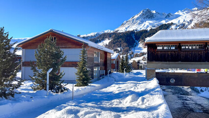Traditional wooden buildings and trees covered in fresh snow with a mountain peak rising majestically in the background