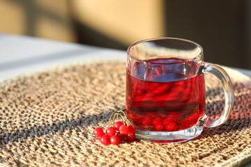 Glass cup of hot viburnum tea on table in living room, closeup