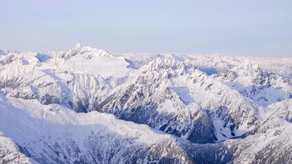 High-altitude panoramic view of rugged, snow-covered mountain ranges under a pale blue winter sky, illustrating an arctic landscape © HABI ANGGARA PUTRA