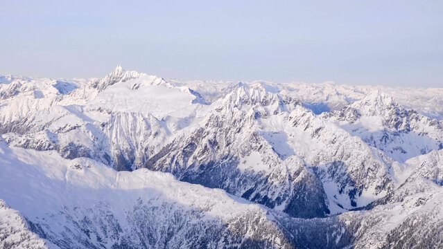 High-altitude panoramic view of rugged, snow-covered mountain ranges under a pale blue winter sky, illustrating an arctic landscape - Powered by Adobe