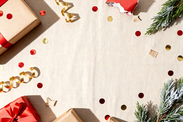 After Christmas flat lay with scattered red-and-gold confetti, torn gift wrap pieces, ribbon curls on beige linen background with copy space for text or design