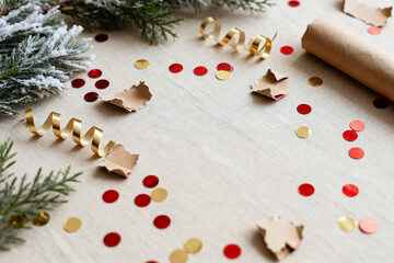 Minimalist after-Christmas flat lay featuring scattered red and gold confetti, curled ribbons, torn wrapping paper pieces on beige linen with copy space for greeting