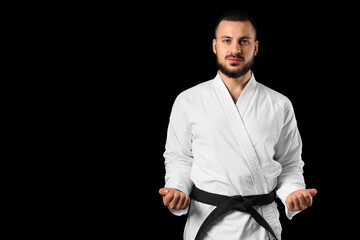Obraz premium Young man practicing karate on black background