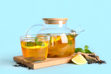 Glass teapot and cup of tasty fruit tea on blue background, closeup