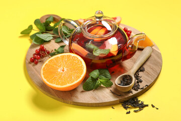 Wooden board with glass teapot of tasty fruit tea and ingredients on yellow background, closeup