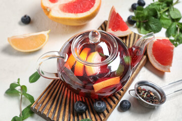 Teapot with tasty fruit tea and ingredients on white grunge background, closeup