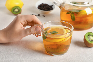 Female hand with cup of tasty fruit tea on white grunge background, closeup