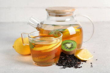 Teapot with tasty fruit tea, cup and ingredients on white grunge table, closeup