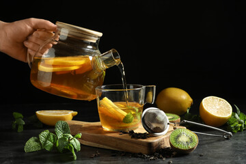 Young woman pouring hot fruit tea into glass cup on black grunge table