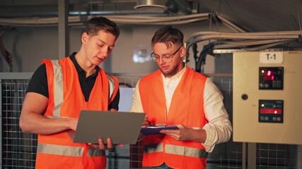 Two dedicated electricians engineers meticulously analyze data on a laptop while consulting control panel. Professional collaboration showcasing teamwork, expertise, and digital innovation.