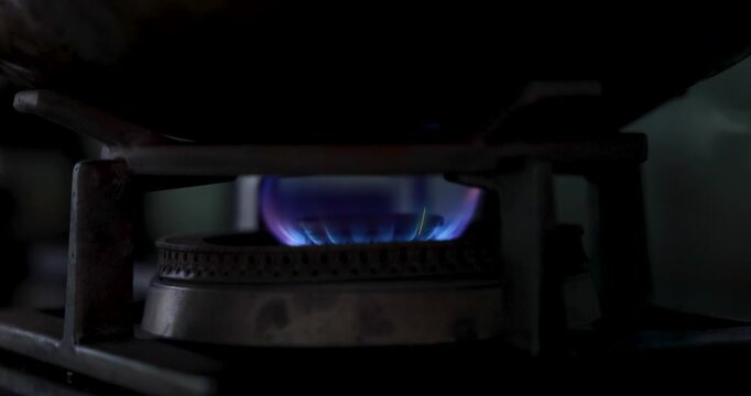 Close up view of blue fire flame burning on gas stove burner. Detail of natural gas igniting under wok for cooking food in kitchen. 4K video household appliance background.