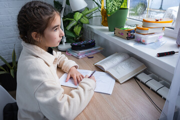 A schoolgirl girl prepares homework for school at the table