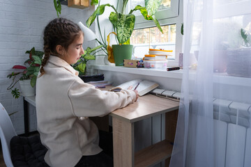 A schoolgirl girl prepares homework for school at the table