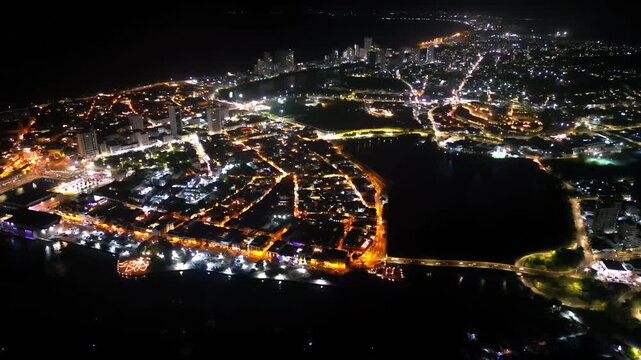 Aerial drone view of Cartagena at night showing both the colonial old town and the modern skyline glowing with orange and white lights