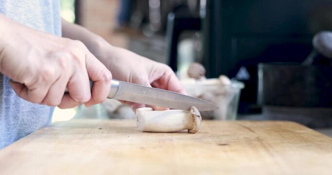 Close up hands using sharp knife to slice fresh white mushrooms on wooden cutting board. Chef preparing organic vegetable ingredients for healthy cooking. High quality 4K video.