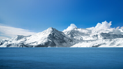 Stunning view of snow-capped mountains with surface of a blue lake and clear blue sky. Natural background