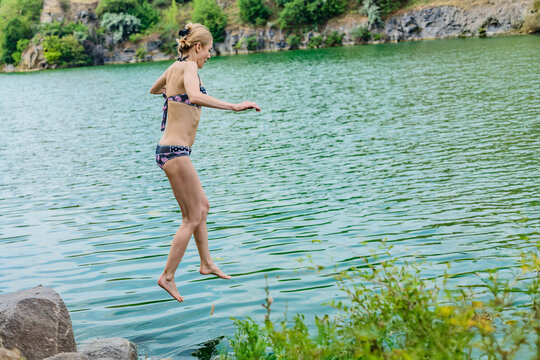 Young woman in bikini jumping off a cliff to the lake on summer sunny day. Girl mid-air while leaping into water, active summer lifestyle moment