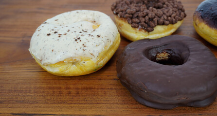 donuts with chocolate topping, chocolate cereal, and a bomboloni with vanilla topping, on a brown wooden table