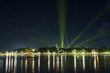 Dramatic green spotlights fan out over the Perfume River at night, illuminating boats and reflecting on the dark water surface.