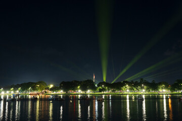 Dramatic green spotlights fan out over the Perfume River at night, illuminating boats and reflecting on the dark water surface.