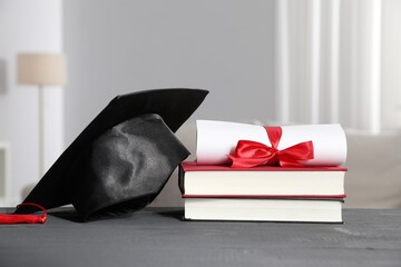 Diploma, graduation hat and books on grey wooden table indoors