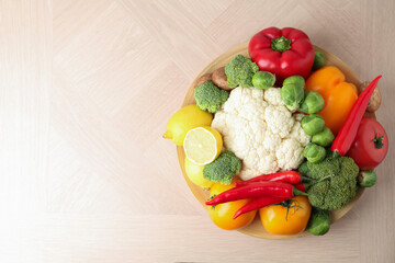 Different fresh raw vegetables and fruits in bowl on wooden table, top view. Space for text