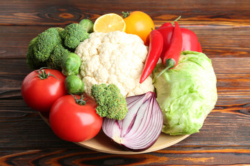 Different fresh raw vegetables and fruits in bowl on wooden table, closeup