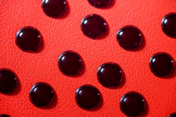 Closeup view of black fluid drops on a textured red background