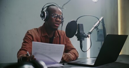 African American Male Expert Content Creator in Studio Records Podcast, Using Prepared Notes and Professional Audio Gear. Concept of Knowledge Sharing and Production of Expert Driven Digital Media.