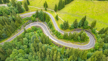 Winding asphalt roads snake through the green Alps, creating breathtaking views for travelers on an adventurous road trip, perfect for drone enthusiasts looking for stunning aerial perspectives.
