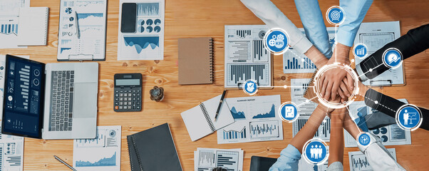 Aerial view of diverse hands stacking together on a wooden desk with laptops, charts, and graphs,...