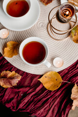 Elegant white cups with black tea on a burgundy cloth, paired with cake and candles for a calm cozy atmosphere.