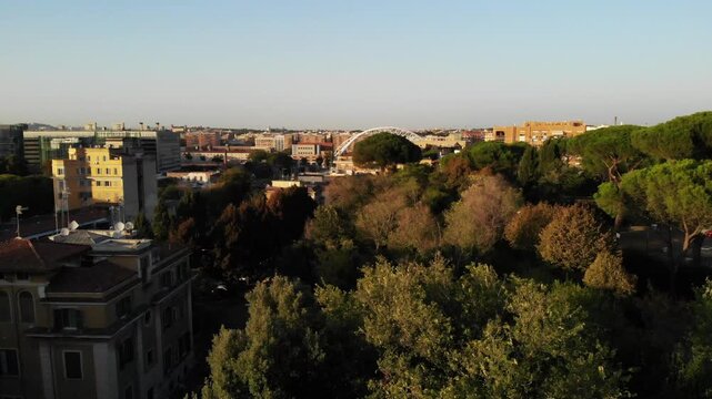 Drone aerial over a green area in Garbatella, Rome, during autumn at sunset. Golden light, fall colors, trees, and residential buildings in view