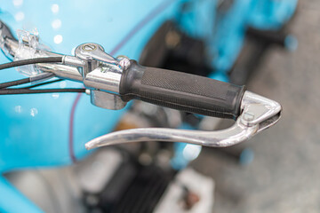 Obraz premium Close-up view of a vintage blue motorcycle handlebar with black grips, turn signal, brake light, and artificial lighting in an indoor setting