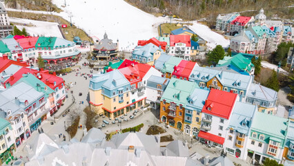 An aerial view of a vibrant, colorful pedestrian village resort in a snowy mountain area, featuring red, blue, and green roofs