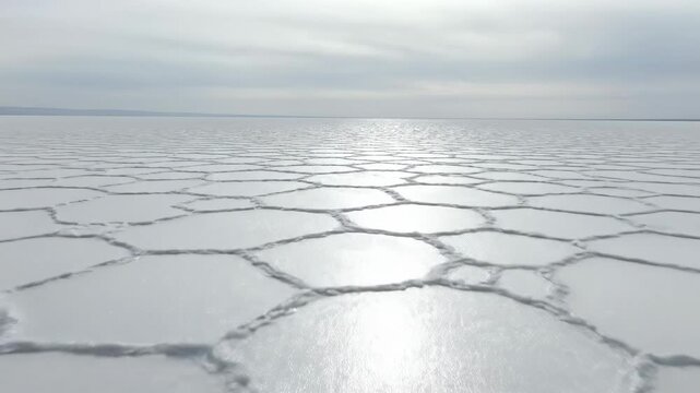 Stunning wide drone shot sweeping slowly over a massive, desolate salt flat stretching to the horizon under a pale, featureless sky blank space, vast landscape, wide drone shot