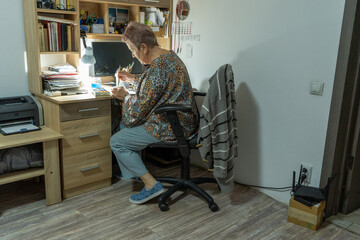 An elderly woman paints with watercolors at home. Grandmother hobby drawing. Craft work table