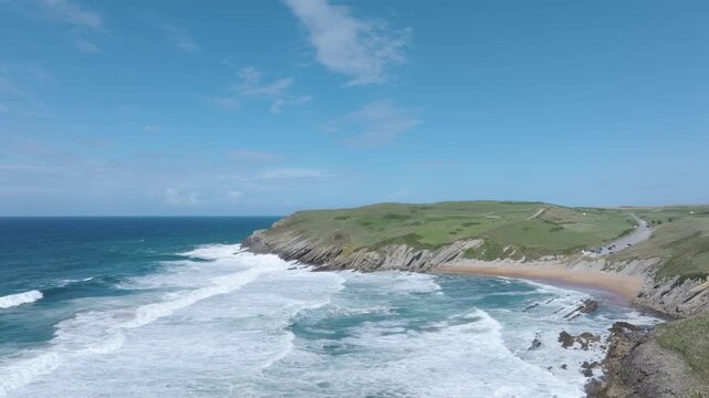 Slow-motion drone flight along the Cantabrian coast at sunset, showcasing the powerful sea, the stunning Tagle beach, and the dramatic cliffs where the ruined 14th-century tower of San Telmo stands.