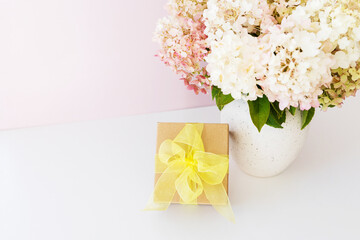 Gift box with yellow bow and beautiful bouquet of white hydrangeas flowers on white background. Gift for holiday, birthday, Wedding, Mother's Day, Valentine's day, Women's Day. Floral arrangement