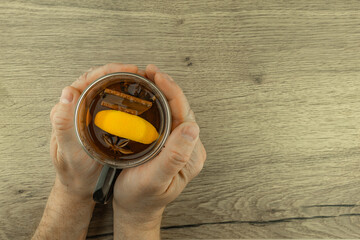 A man warms his cold hands with a clear double-walled glass filled with hot tea with oriental spices, cinnamon sticks, hibiscus, cloves, orange, star anise,