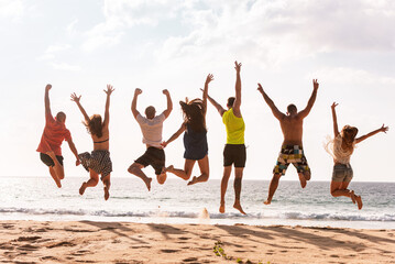 Big group of happy young friends are having fun and jumping at sunset sea beach
