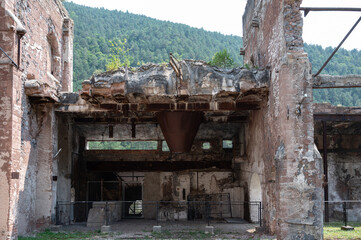 Detail of the crumbling facade of an old cement factory in Castellar de n'Hug, showcasing a rusty industrial hopper, exposed metal beams, and severe decay.