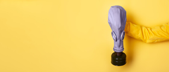 A person in a yellow sleeve holds a gas mask against a vibrant yellow background, symbolizing...