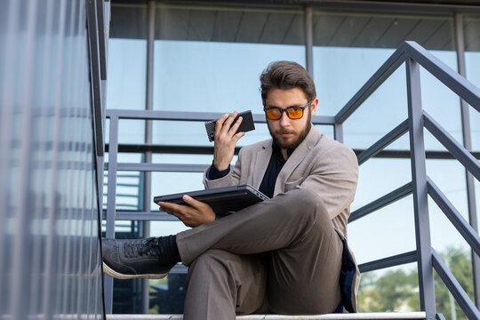 A man is sitting on a set of outdoor stairs, looking at a tablet or laptop