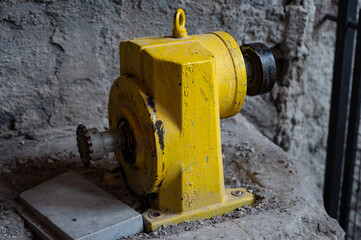 Close-up of a heavy-duty yellow industrial gear reducer (gearbox) with a sprocket for a chain drive, abandoned on a stone floor in an old factory