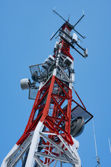 Low-angle close-up of a massive red and white telecommunications tower, heavily loaded with parabolic dishes and antennas for radio and television signal transmission.