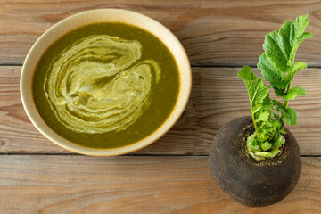 Freshly harvested raw winter radish and a plate with winter radish leaf soup on a rustic wooden table. 